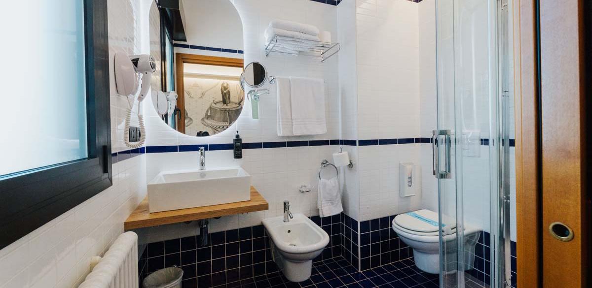 Bagno moderno, elegante, con piastrelle blu e bianche, doccia e specchio luminoso.